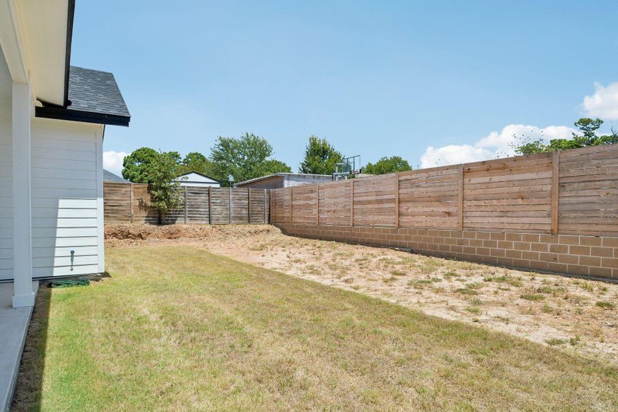 A wooden privacy fence surrounds the grassy backyard space under clear blue skies. A wooden privacy fence surrounds the grassy backyard space under clear blue skies.