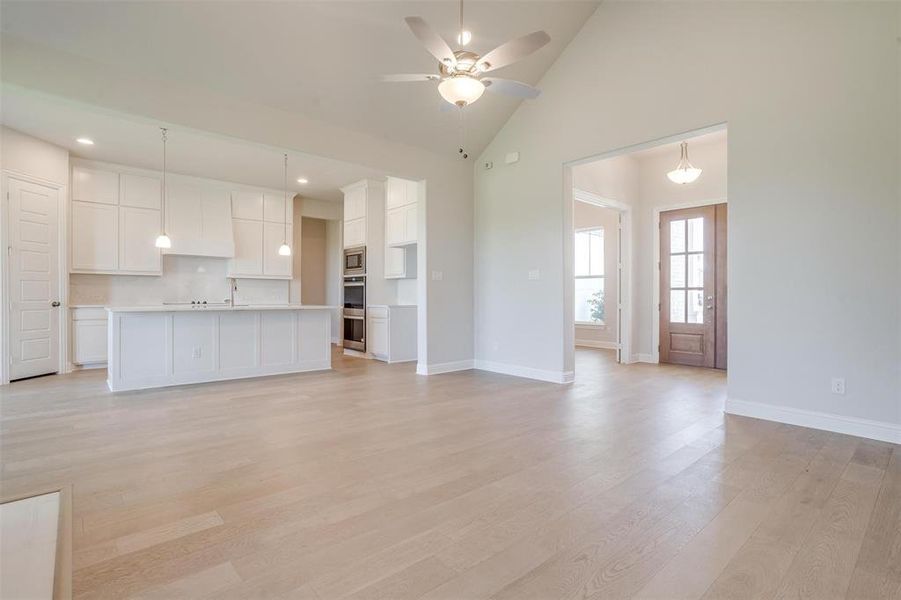 Unfurnished living room featuring sink, light hardwood / wood-style flooring, ceiling fan, and high vaulted ceiling