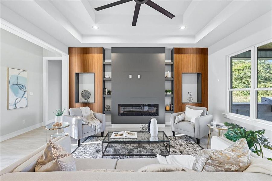 Living room with a glass covered fireplace, a raised ceiling, recessed lighting, a ceiling fan, and built in shelves Living room with a glass covered fireplace, a raised ceiling, recessed lighting, a ceiling fan, and built in shelves