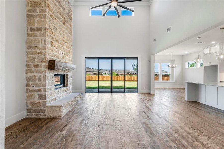 Unfurnished living room featuring a towering ceiling, dark hardwood / wood-style flooring, ceiling fan with notable chandelier, and a stone fireplace