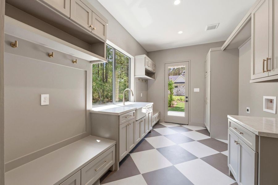 Elegant MOODY laundry room showcasing custom built-ins/ drop off zones, PORCELAIN sink, and DESIGNER gray and white checkered tile flooring.