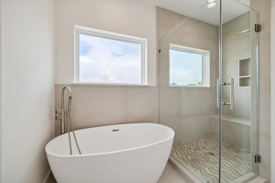 The primary bath delivers a luxurious spa-like experience with a sculptural freestanding soaking tub and an oversized glass-enclosed shower. Neutral large-format tile creates a sleek contemporary backdrop, while patterned shower flooring, built-in niches, and a rainfall-style showerhead add thoughtful detail. A large window fills the space with natural light, and the freestanding tub filler provides an elegant finishing touch to this beautifully designed private retreat. The primary bath delivers a luxurious spa-like experience with a sculptural freestanding soaking tub and an oversized glass-enclosed shower. Neutral large-format tile creates a sleek contemporary backdrop, while patterned shower flooring, built-in niches, and a rainfall-style showerhead add thoughtful detail. A large window fills the space with natural light, and the freestanding tub filler provides an elegant finishing touch to this beautifully designed private retreat.