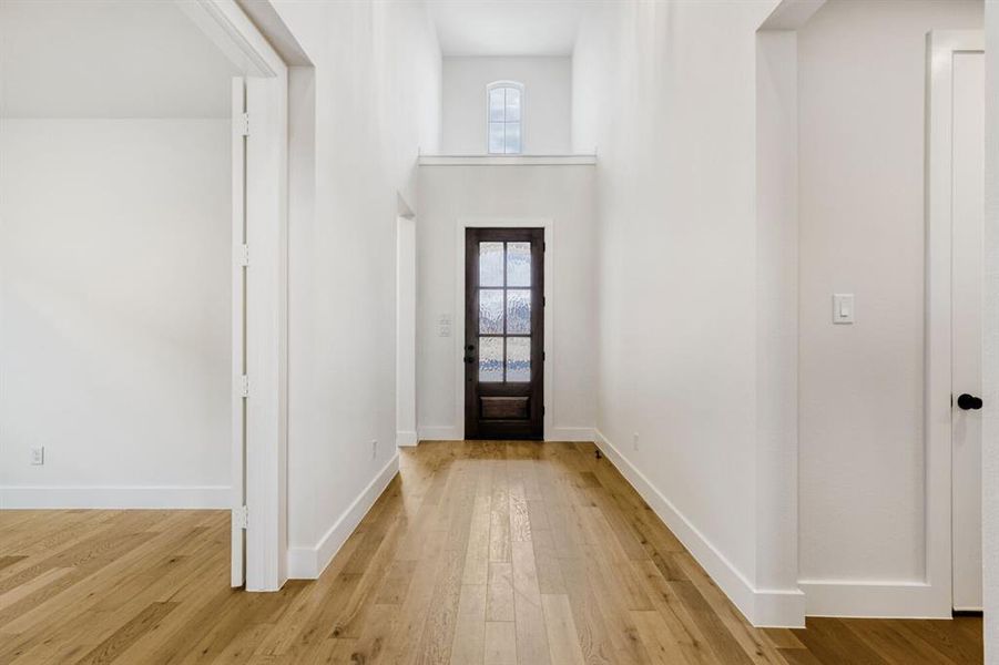 Entryway featuring vaulted ceilings, wood-finish flooring, a dark wood door with privacy glass, white baseboards, and bright white walls