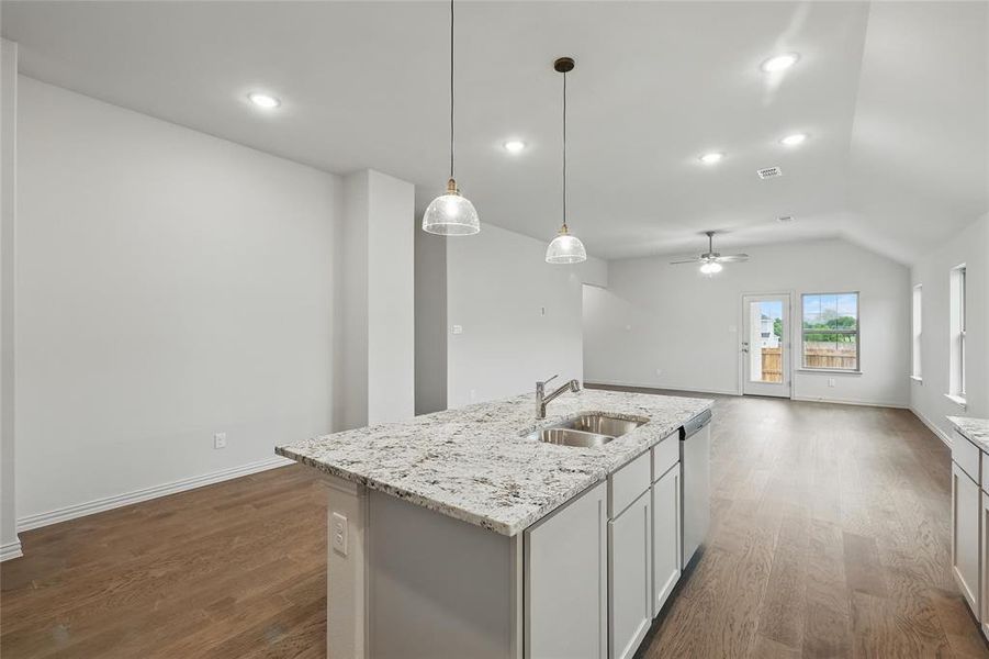 Kitchen with light stone counters, a center island with sink, dark wood finished floors, open floor plan, and a ceiling fan