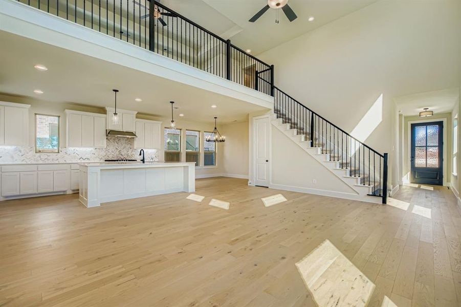 Unfurnished living room featuring light wood-type flooring, a chandelier, stairs, recessed lighting, and a high ceiling