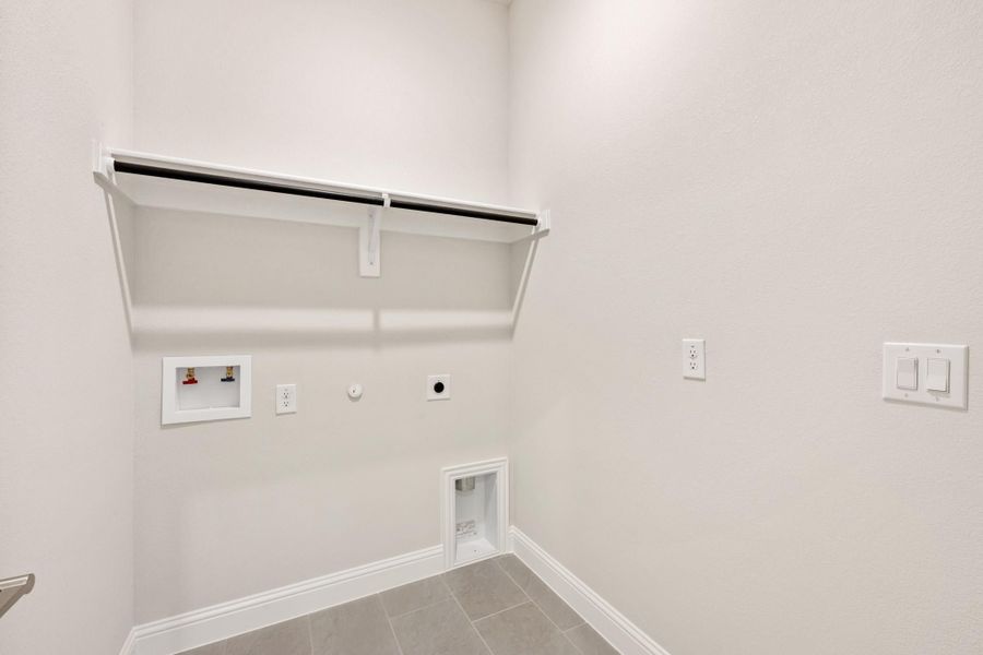 Laundry room with wall-mounted shelf, hanging rod, washer hookups, and dryer vent on tile floor Laundry room with wall-mounted shelf, hanging rod, washer hookups, and dryer vent on tile floor