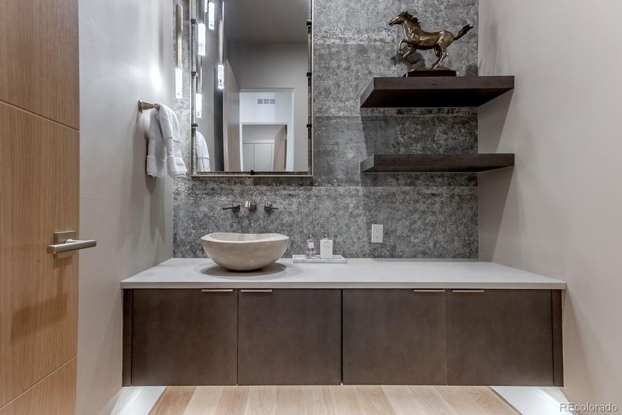 The main-level powder bath makes a bold impression: a floating vanity beneath decorative lighting, an artisanal stone sink, and a textured tile accent wall. Every surface feels curated for visual impact and tactile delight.