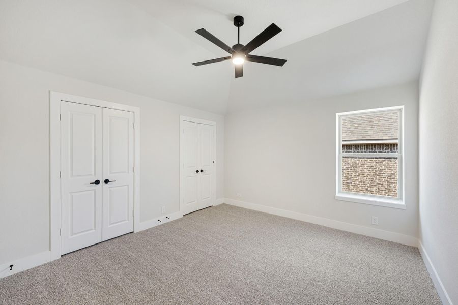 Empty bedroom with carpet, vaulted ceiling, black ceiling fan, and two white closet doors