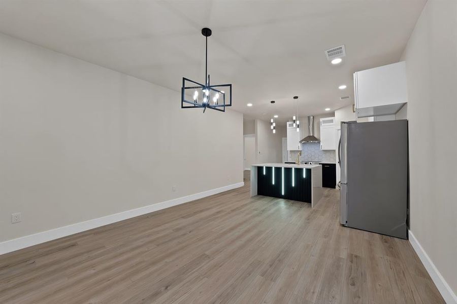 Kitchen with freestanding refrigerator, white cabinets, hanging light fixtures, a center island with sink, and recessed lighting