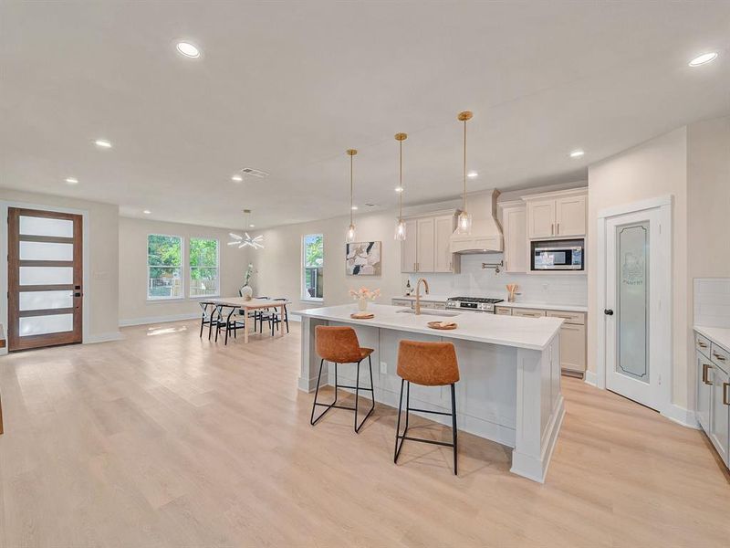 Kitchen with a large island with sink, premium range hood, pendant lighting, and white cabinets