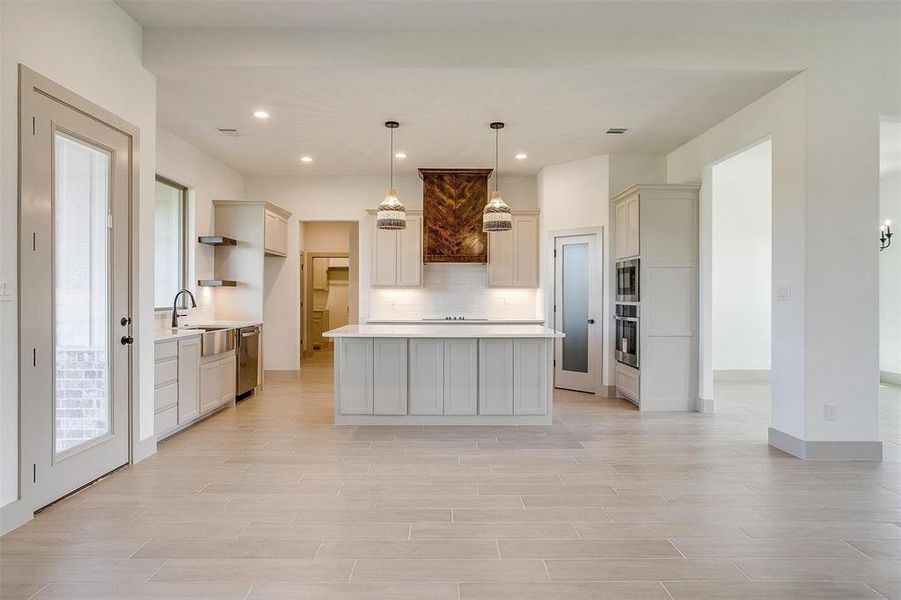 Kitchen featuring decorative backsplash, hanging light fixtures, dishwasher, sink, and a center island