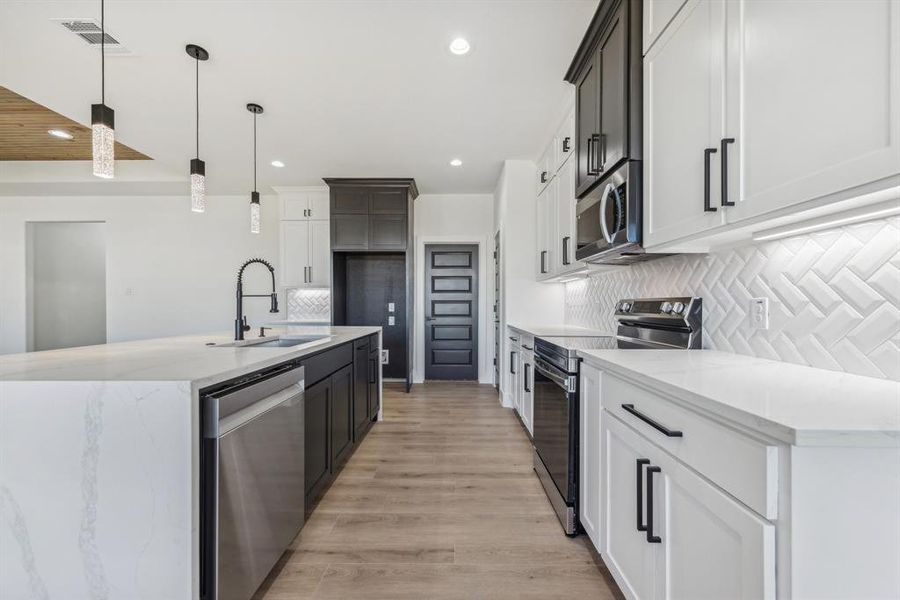 Kitchen featuring sink, appliances with stainless steel finishes, pendant lighting, white cabinets, and light wood-type flooring