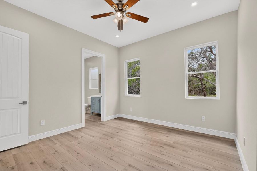 Smooth wood-look flooring and tall windows framed by neutral walls define this secondary bedroom.