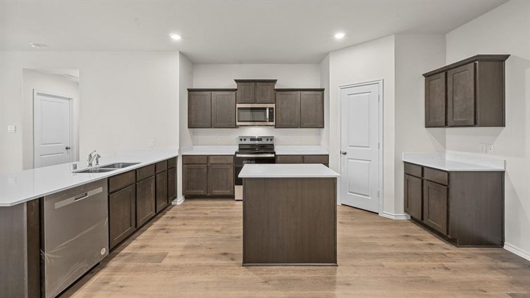 Kitchen with stainless steel appliances, a center island, dark wood finish cabinetry, a peninsula, and light wood finished floors