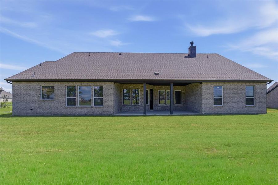 Expansive rear exterior featuring a covered patio, multiple large windows, a brick veneer finish, and a dark shingle roof Expansive rear exterior featuring a covered patio, multiple large windows, a brick veneer finish, and a dark shingle roof
