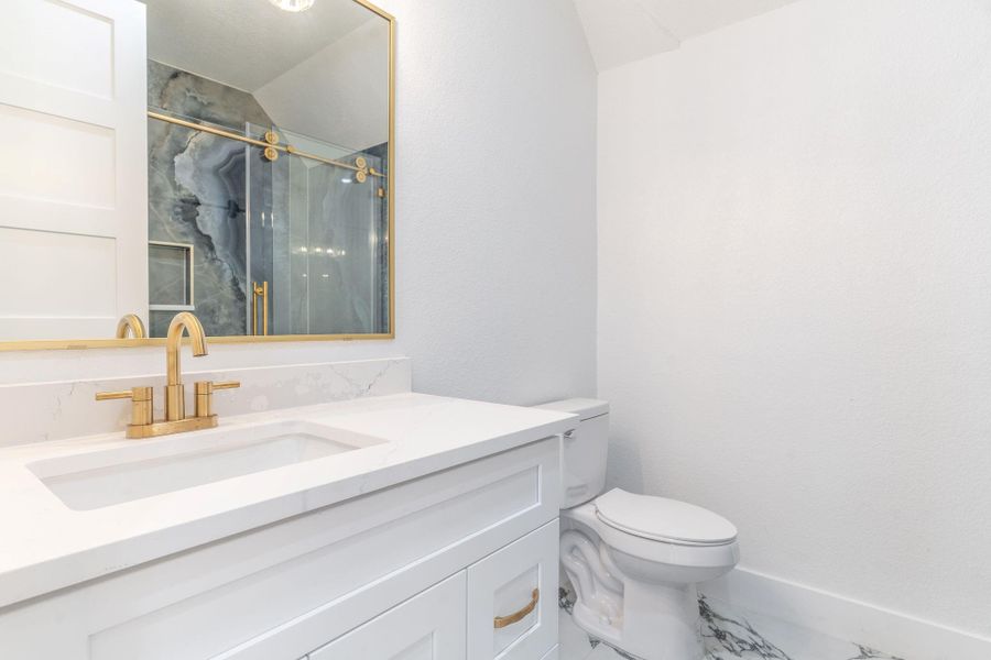 A masterpiece of bath design, this shower features stunning book-matched stone slabs with intricate natural veining. Professional-grade brushed gold hardware and a frameless glass enclosure create a high-end, spa-like experience.