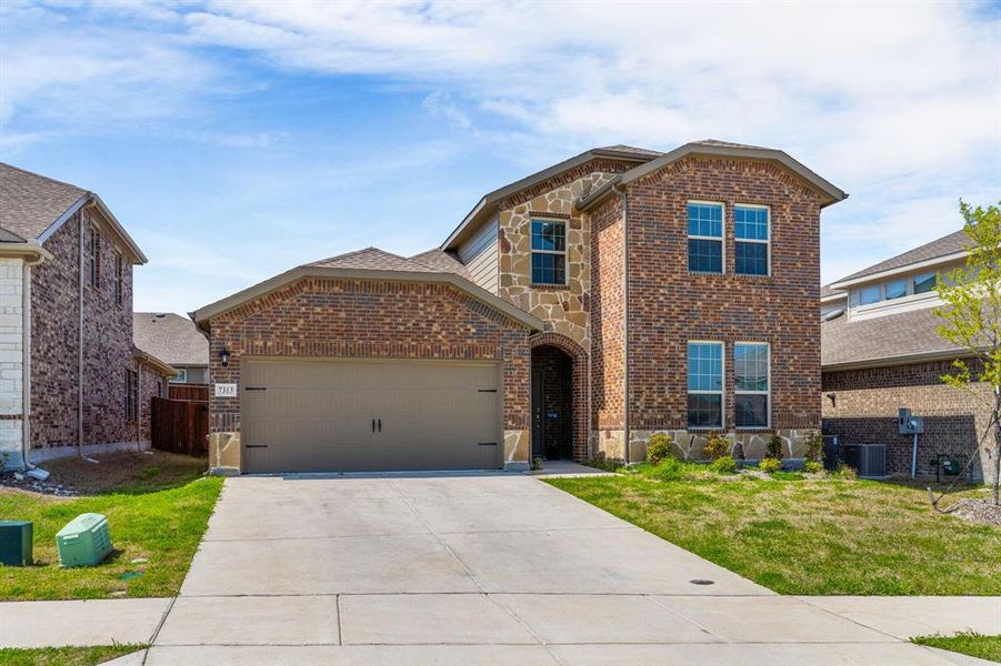Traditional-style house with stone siding, driveway, a front yard, brick siding, and a garage Traditional-style house with stone siding, driveway, a front yard, brick siding, and a garage