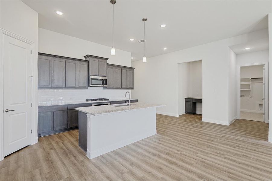 Kitchen featuring pendant lighting, backsplash, sink, an island with sink, and light stone counters