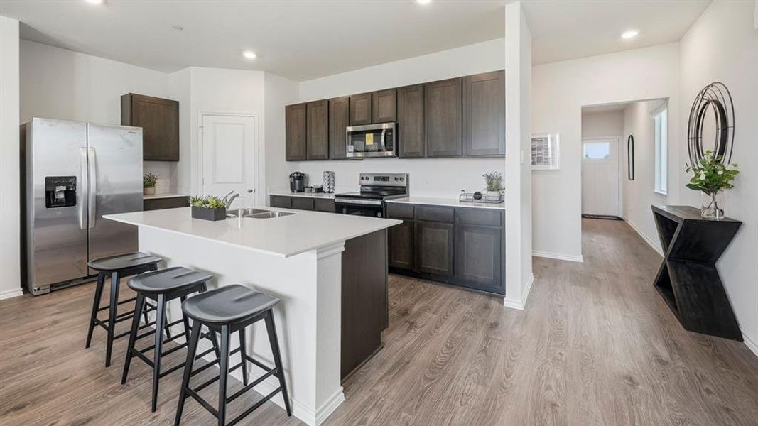 Kitchen featuring dark brown cabinets, appliances with stainless steel finishes, a kitchen breakfast bar, light wood-type flooring, and recessed lighting Kitchen featuring dark brown cabinets, appliances with stainless steel finishes, a kitchen breakfast bar, light wood-type flooring, and recessed lighting
