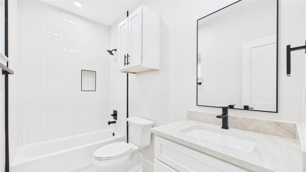 This bathroom features a modern design with a sleek white vanity, black fixtures, and a large mirror. It includes a bathtub with a built-in niche and bright tile walls, creating a clean and spacious feel.