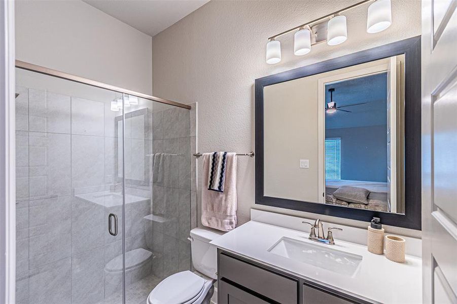 Bathroom featuring a glass-enclosed shower with tiled walls, a white vanity with an integrated rectangular sink, a framed mirror, and a four-light fixture