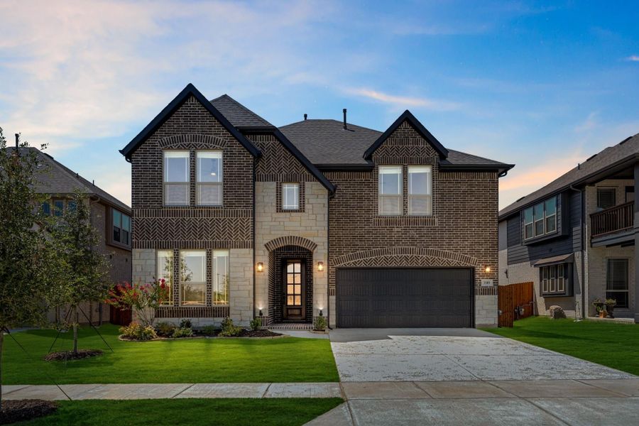 Two-story brick home with stone accents, two-car garage, arched entry, and manicured front lawn at dusk