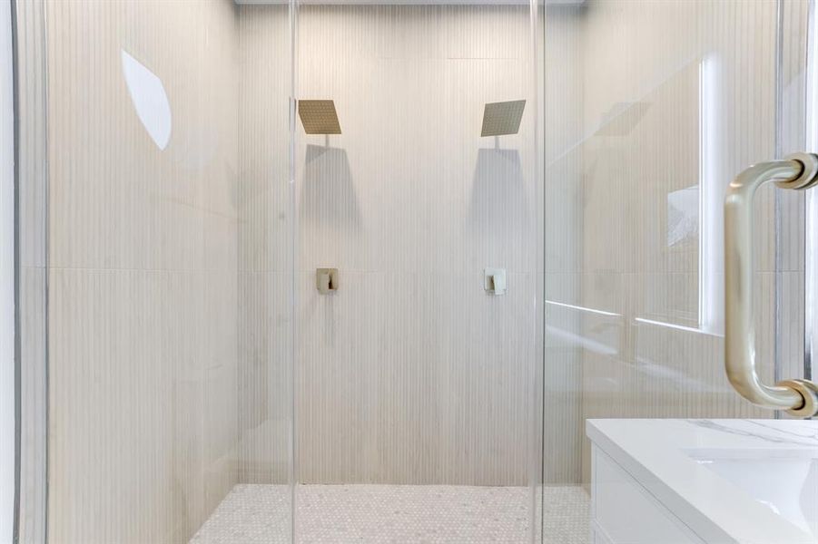 Gorgeous frameless walk-in shower with golden dual shower heads and elegant neutral toned shower tiles.