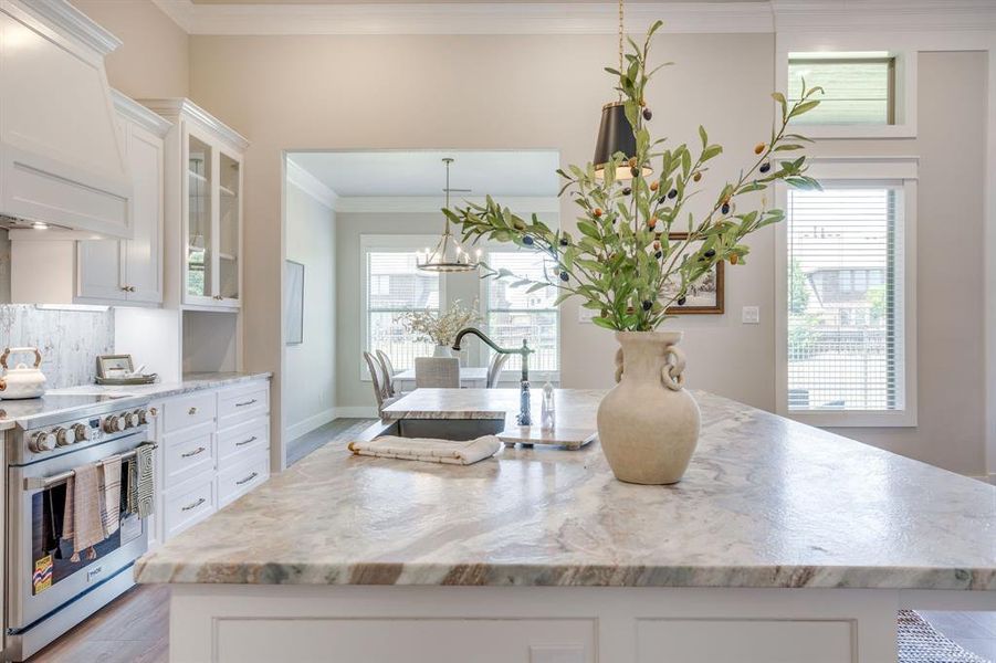 Kitchen island featuring a single-basin sink with a gooseneck faucet, light-toned stone countertop, and pendant lighting