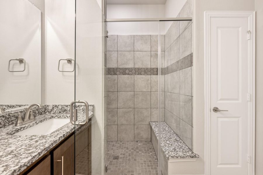 Bathroom with glass walk-in shower, gray tile walls, built-in bench, and granite vanity countertop