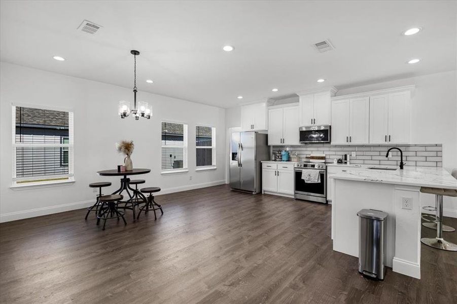 Kitchen featuring tasteful backsplash, a peninsula, recessed lighting, a breakfast bar area, and white cabinetry Kitchen featuring tasteful backsplash, a peninsula, recessed lighting, a breakfast bar area, and white cabinetry