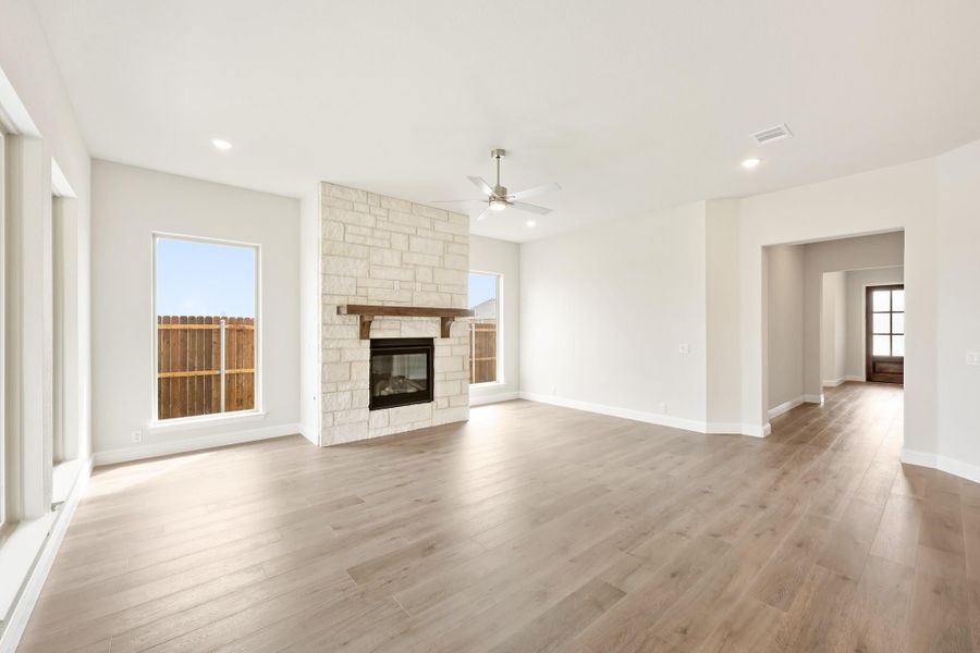 Open living room with stone fireplace, wood mantel, hardwood floors, and ceiling fan