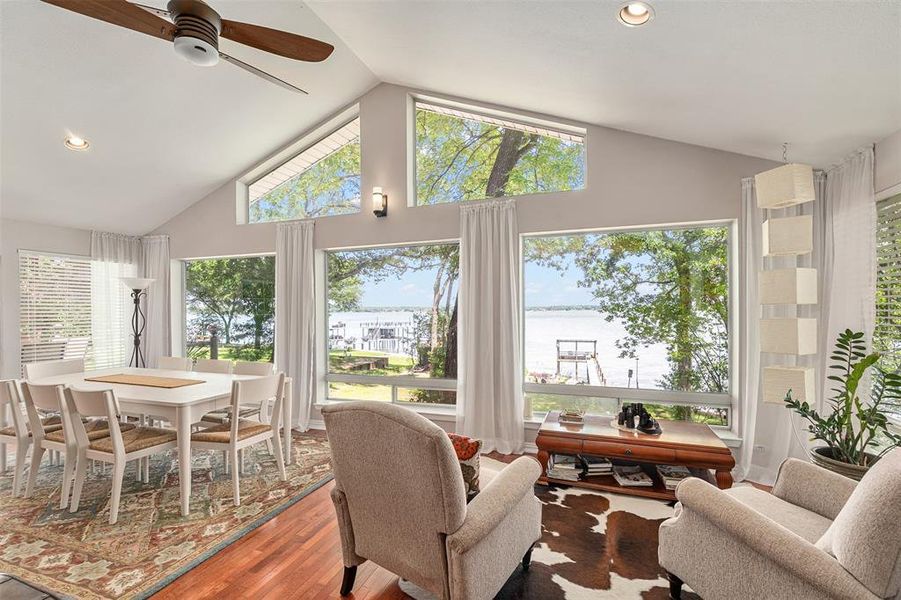 Vaulted ceiling living area featuring wood-finish flooring and expansive windows overlooking a body of water