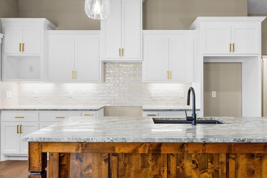 Kitchen with white cabinets, tasteful backsplash, light stone counters, and pendant lighting Kitchen with white cabinets, tasteful backsplash, light stone counters, and pendant lighting