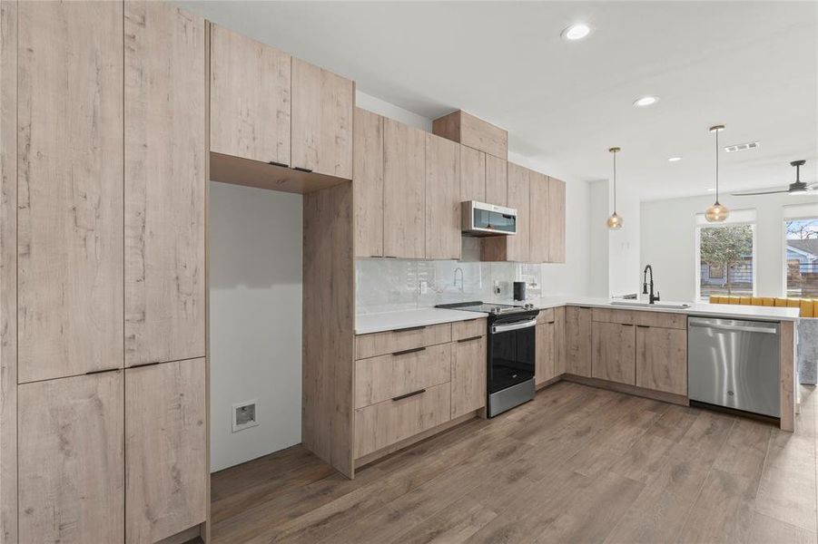 Kitchen featuring wood-type flooring, pendant lighting, decorative backsplash, light brown cabinetry, and appliances with stainless steel finishes