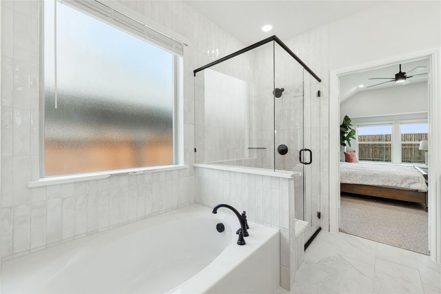 White tiled ensuite bathroom with soaking tub, glass-enclosed shower, and view into master bedroom