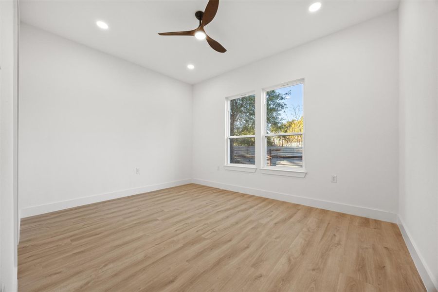 Bright and airy room with large windows, wood-like flooring, and a modern ceiling fan. Ideal for a bedroom or office space.