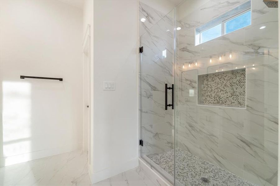 A gorgeous stand alone shower boasting a frameless glass door, lovely penny tile flooring and a large soap niche.