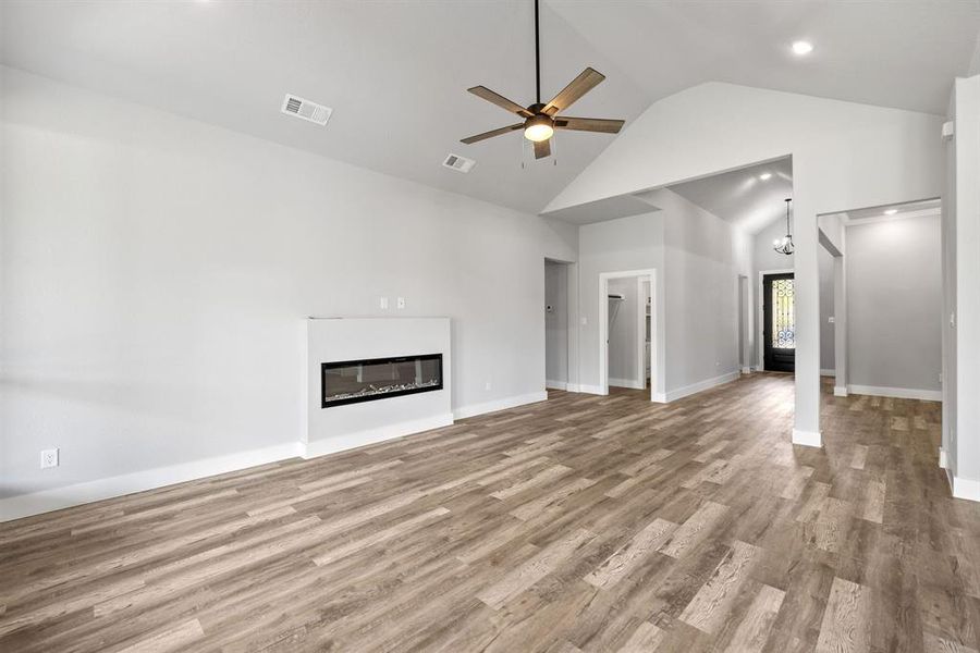 Unfurnished living room with a glass covered fireplace, wood finished floors, a ceiling fan, high vaulted ceiling, and a chandelier