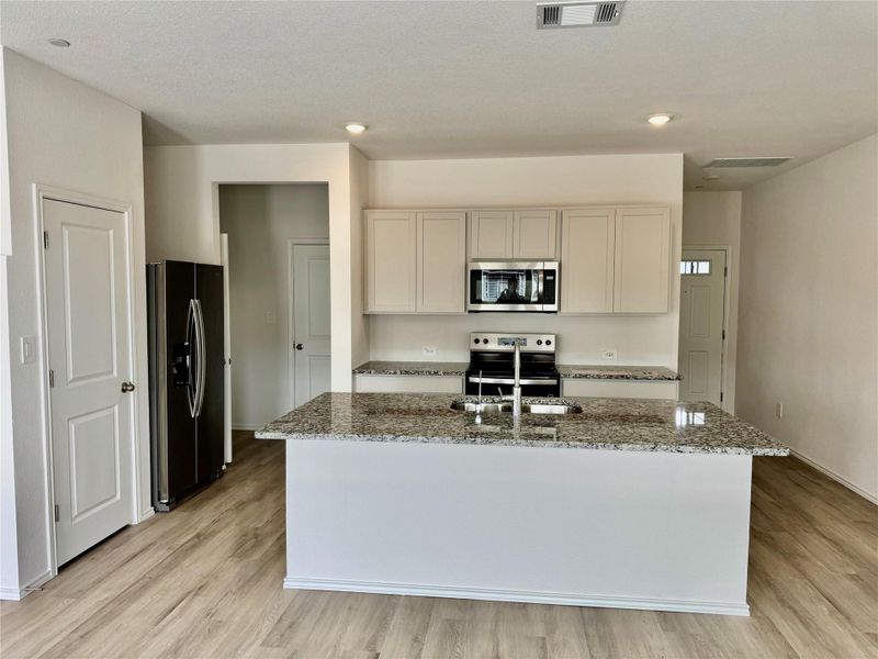 Kitchen featuring light stone counters, stainless steel appliances, light wood finished floors, a kitchen island with sink, and recessed lighting