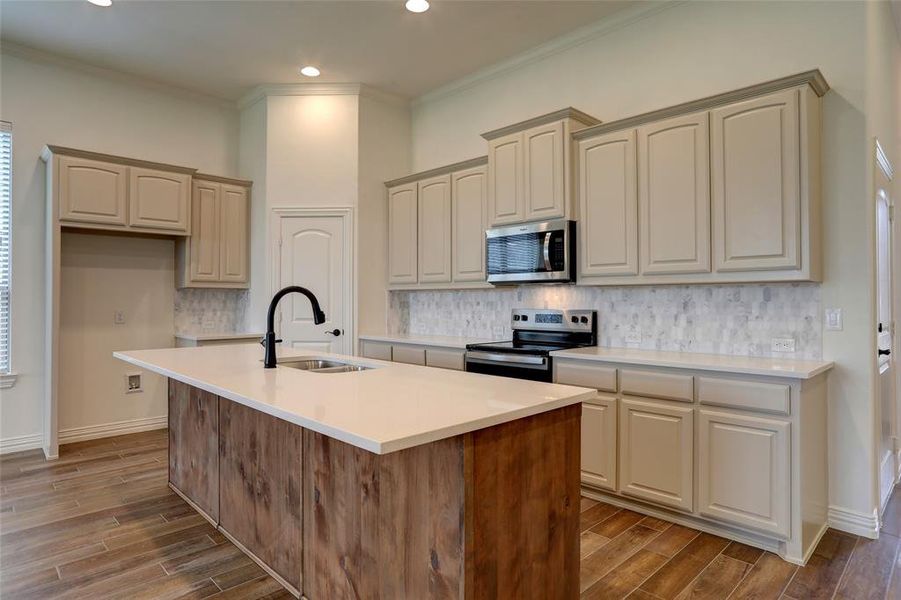 Kitchen featuring stainless steel appliances, backsplash, an island with sink, wood-type flooring, and sink