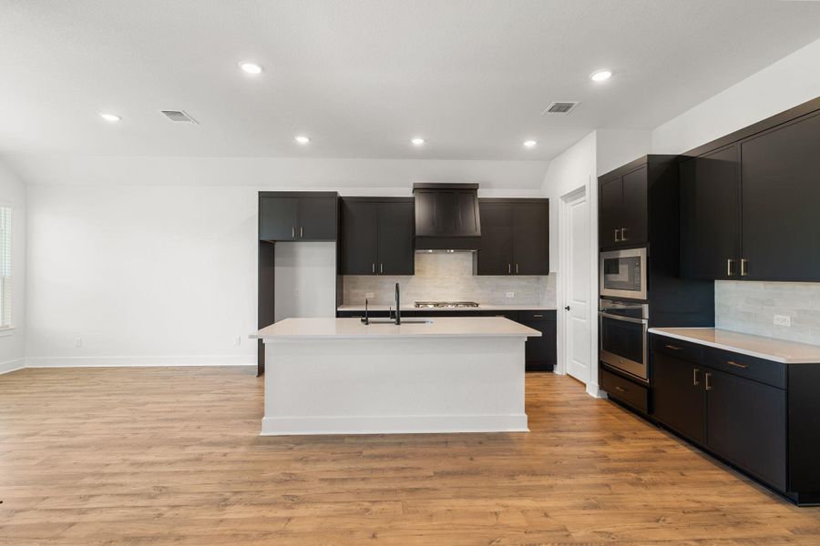 A kitchen showcasing a central island and contemporary black cabinetry, flowing into an open living area.