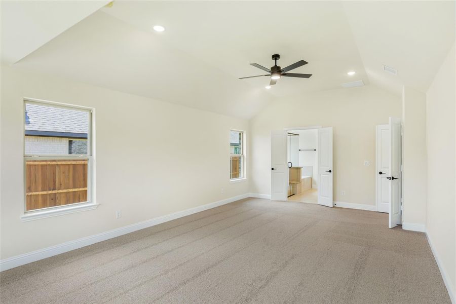 Empty bedroom with vaulted ceiling, ceiling fan, carpet flooring, and open door to ensuite bathroom Empty bedroom with vaulted ceiling, ceiling fan, carpet flooring, and open door to ensuite bathroom