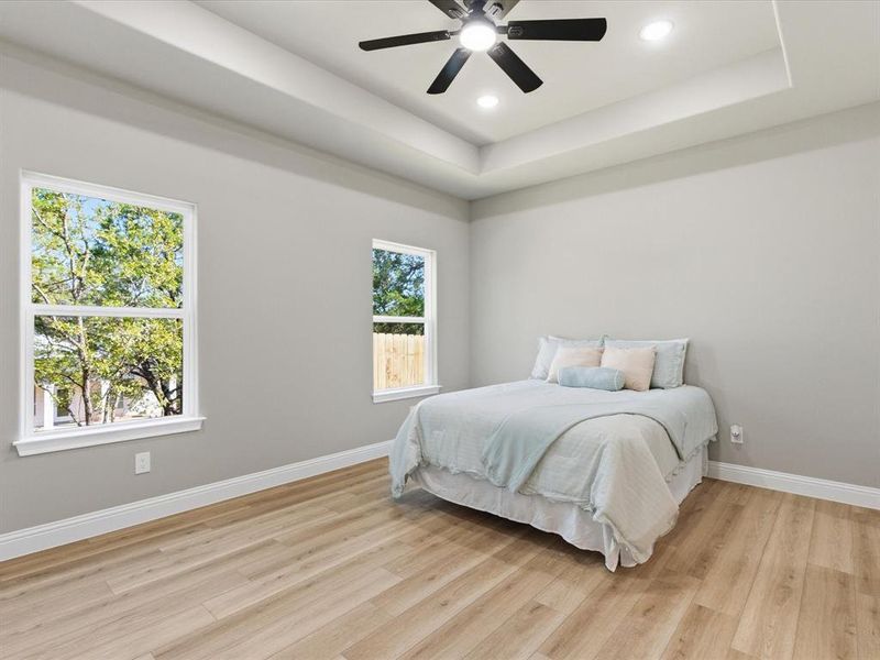 Bedroom with a raised ceiling, light wood-style floors, ceiling fan, and recessed lighting Bedroom with a raised ceiling, light wood-style floors, ceiling fan, and recessed lighting