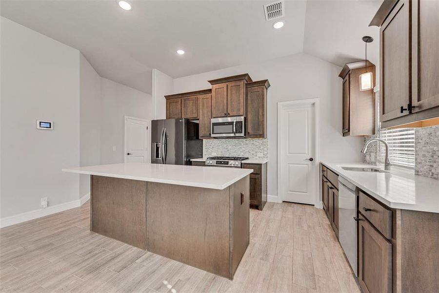 Kitchen featuring tasteful backsplash, a kitchen island, stainless steel appliances, pendant lighting, and light wood finished floors Kitchen featuring tasteful backsplash, a kitchen island, stainless steel appliances, pendant lighting, and light wood finished floors