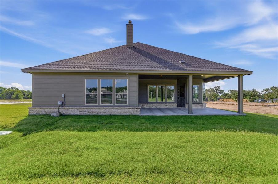 Rear exterior featuring a covered patio, dark gray siding, and a partial stone facade Rear exterior featuring a covered patio, dark gray siding, and a partial stone facade