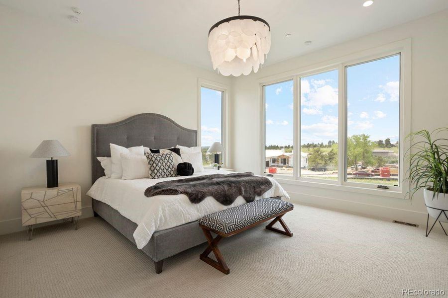 Bright and airy primary bedroom with expansive windows, plush carpeting, and a statement chandelier.