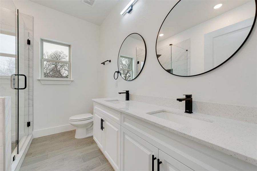 Full bathroom featuring double vanity, a stall shower, baseboards, and a sink