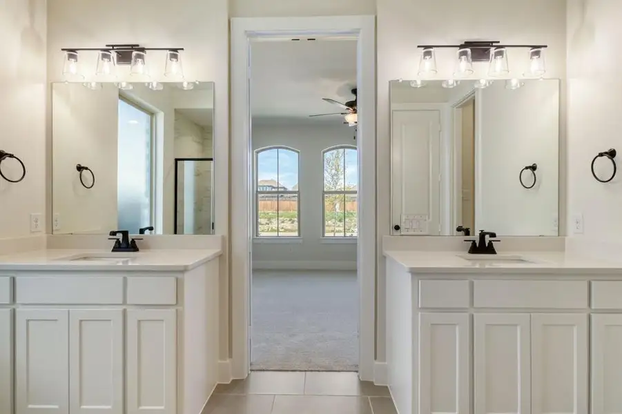 Full bathroom featuring two vanities, ceiling fan, light carpet, light tile patterned flooring, and a stall shower Full bathroom featuring two vanities, ceiling fan, light carpet, light tile patterned flooring, and a stall shower