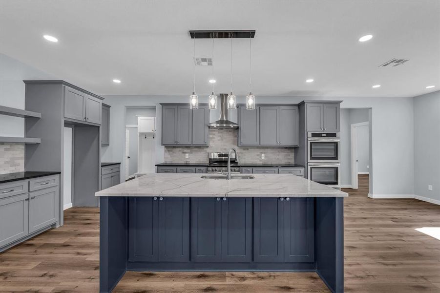 Kitchen with gray cabinetry, decorative backsplash, dark stone counters, wall chimney exhaust hood, and recessed lighting Kitchen with gray cabinetry, decorative backsplash, dark stone counters, wall chimney exhaust hood, and recessed lighting
