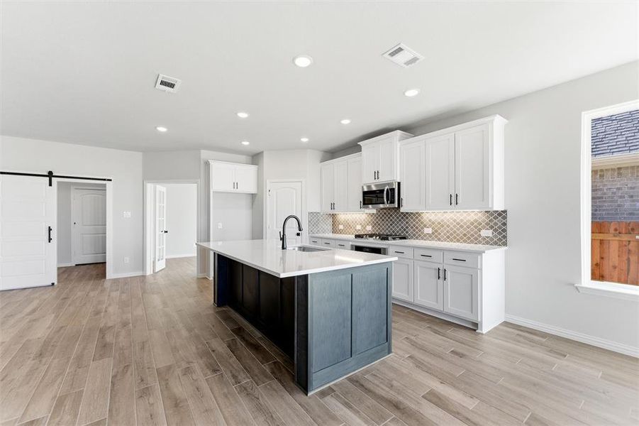Kitchen with a barn door, white cabinetry, a center island with sink, light wood finished floors, and a kitchen breakfast bar